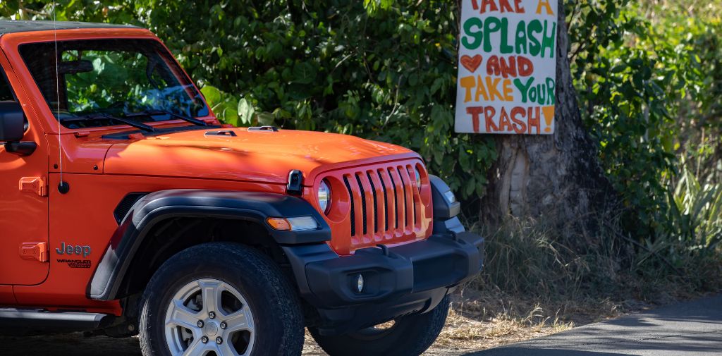 Rental Jeep at a St. Croix beach with a sign reading: Take a splash and take your trash!